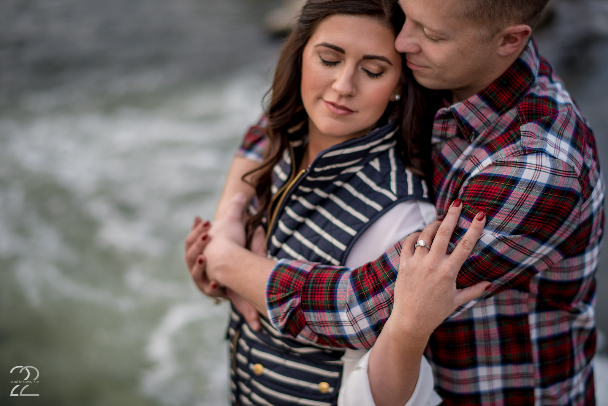 Woman reaches back and touches a man, who has his arms wrapped around her near a river at Eastwood Metropark by Dayton Wedding Photographer Studio 22 Photography